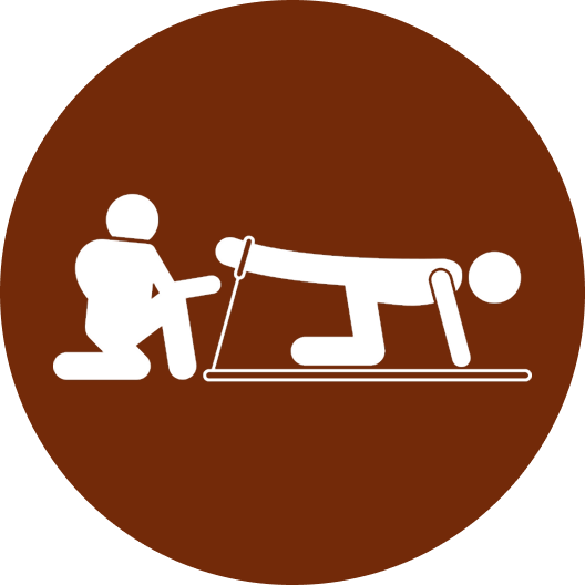 A physiotherapy session showing a person lying on their stomach on a mat, with a physiotherapist assisting them in a leg raise exercise. The physiotherapist is on their knees, supporting the client's raised leg. The client is focused on the exercise while the physiotherapist provides guidance and support.